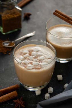 Camda krem şantili sıcak çikolata tarçın çubuğuyla izole edilmiş, koyu arkaplanda.