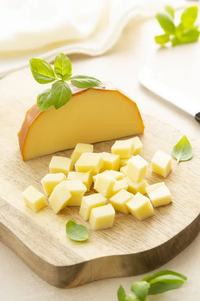 Smoked cheese on cutting board with basil, sliced cheese, dairy product