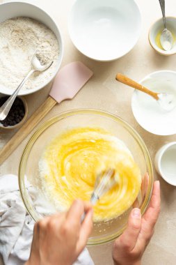 Kadın elleri cam kasede yumurta, şeker, yağ ve yoğurt karıştırıyor. Adım adım kek ya da kek pişirmenin tarifi.