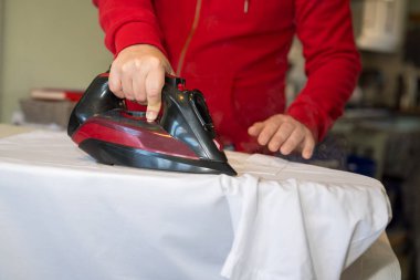 Adamın eli evdeki ütü masasında giysileri ütülüyor. 