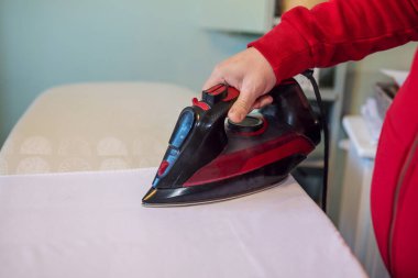 Adamın eli evdeki ütü masasında giysileri ütülüyor. 