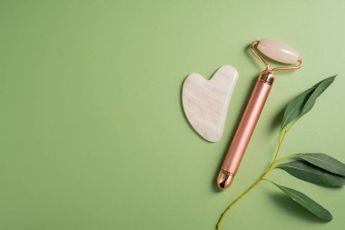 Gua sha aracı ve yüz masajı silindiri yeşil arka planda, güzellik soyut fotoğrafı. Üst görünüm
