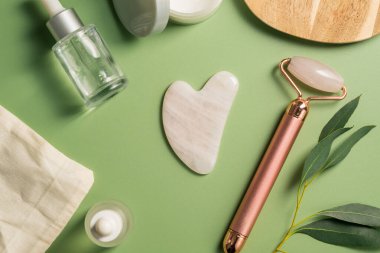 Rose Quartz gua sha aracı ve yeşil arka planda yüz masajı silindiri, güzel soyut fotoğraf. Üst görünüm