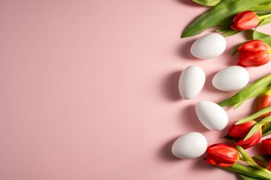 Paskalya, bahar çiçekleri. Kırmızı laleler ve beyaz yumurtalar, pembe arka planda çiçekler.