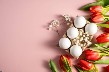 Paskalya, bahar çiçekleri. Kırmızı laleler ve beyaz yumurtalar, pembe arka planda çiçekler.