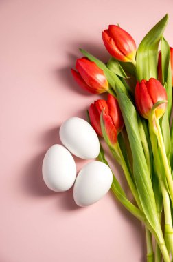 Paskalya tatili geçmişi. Kırmızı laleler ve pembe pastel arka planda Paskalya beyaz yumurtaları, kopyalama uzayı. Düz yatıyordu.