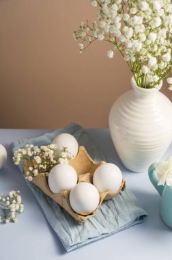 Paskalya yumurtaları. Karton kutuda beyaz yumurtalar ve vazoda çingene çiçekleri. Bahar tatili
