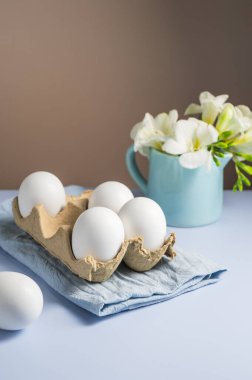 Paskalya yumurtaları ve çiçekler. Karton kutuda beyaz yumurtalar ve Frezya beyaz bahar buketi