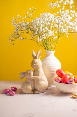Bir kasede paskalya çikolatası renkli yumurtalar, sevimli tavşanlar ve vazoda çingene çiçekleri. Bahar tatili geçmişi.