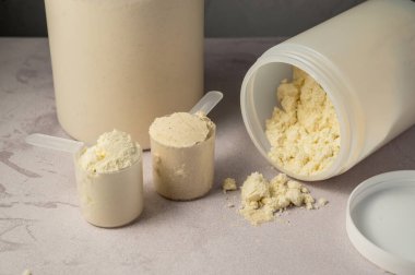 Beyaz plastik protein tüpleriyle kepçelerde protein tozu, arka planda kavanozlar. Vücut geliştirme, kas büyümesi ve gıda takviyesi kavramı