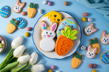 Paskalya bayramı arkaplanda bir tabakta paskalya kurabiyesi: tavşancık, civciv, mavi arka planda havuç ve yumurta, mini çikolatalı yumurta şekerlemeleri