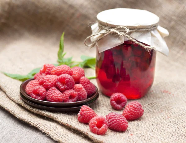 Raspberry preserve in glass jar and fresh raspberries on a plate Stock Picture