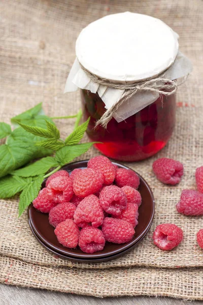 Raspberry preserve in glass jar and fresh raspberries on a plate — Stock Photo, Image