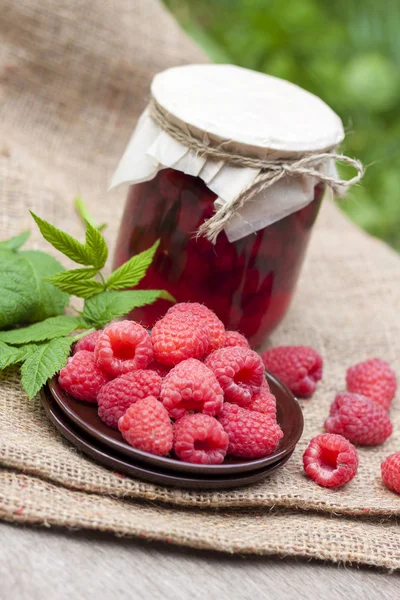覆盆子保存在玻璃罐和新鲜树莓在盘子上 免版税图库照片