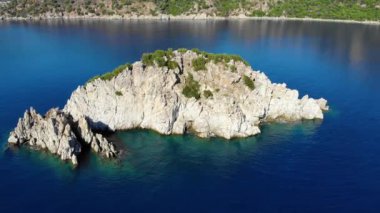 Temiz mavi suyla çevrili küçük kayalık bir adanın etrafındaki hava manzarası. İHA atışı. 4K