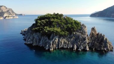 Temiz mavi suyla çevrili küçük kayalık bir adanın üzerinden uç. Yakın çekim görüntüsü. Hava aracı görüntüsü. 4K.