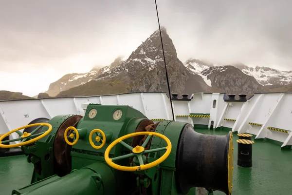 Windlass, dağ ve sisli gökyüzü olan yolcu gemisinin ana güvertesinde. Büyük geminin demirleme vinci.