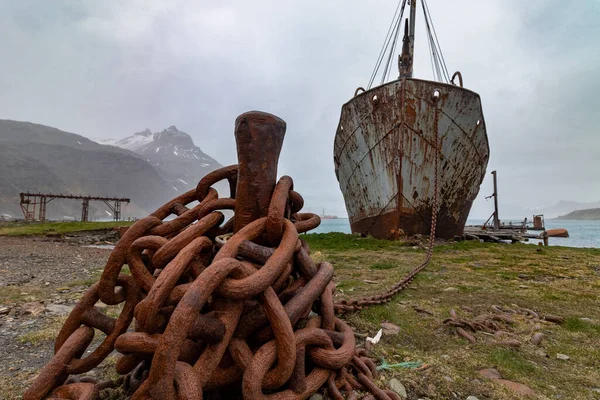 Grytviken 'de terk edilmiş bir balina avlama üssünde ön planda çapa zinciri olan eski paslı bir gemi. Güney Georgia.
