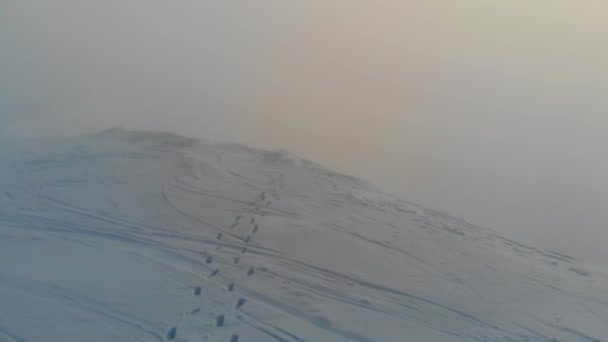 Pegadas humanas que levam a um penhasco na neve fresca no cume da montanha. Vista aérea. — Vídeo de Stock