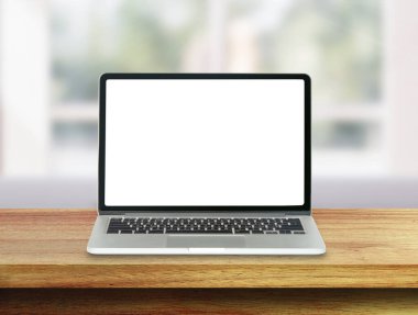 Ahşap masadaki beyaz boş ekranlı dizüstü bilgisayar ve arka plandaki odanın bulanık görüntüsü.