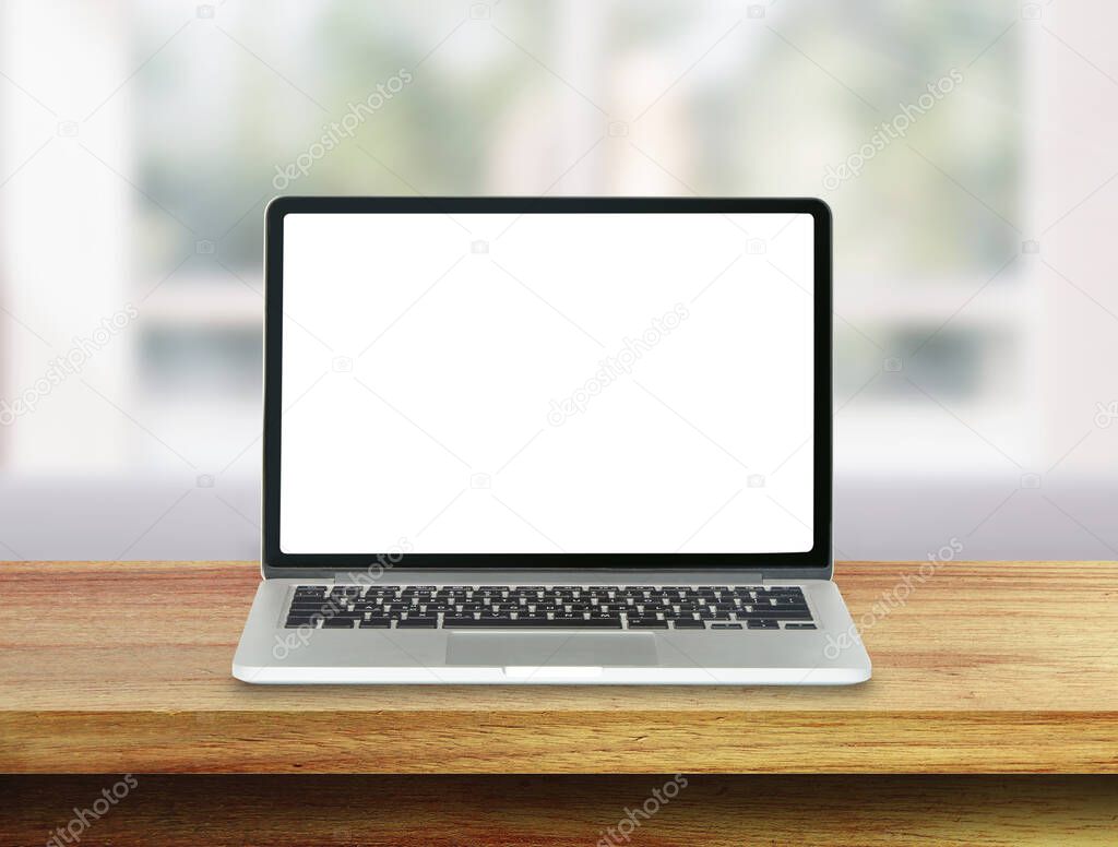 Laptop with white blank screen on wooden table top and blurry image of inside room in background.