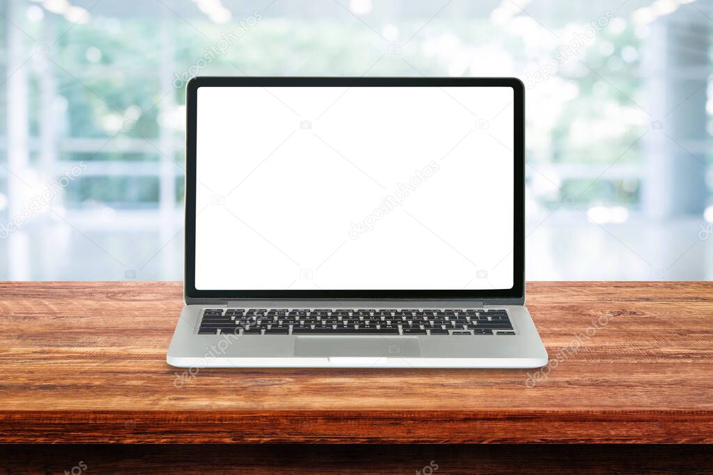 Laptop with white blank screen on wooden table top and blurry image of inside room in background.