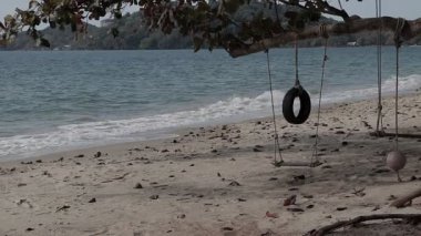 Tayland, Rayong 'da sakin bir plajda sallanan ağaçtan salıncak ve lastik salıncak. Arka planda hafif okyanus dalgaları var..