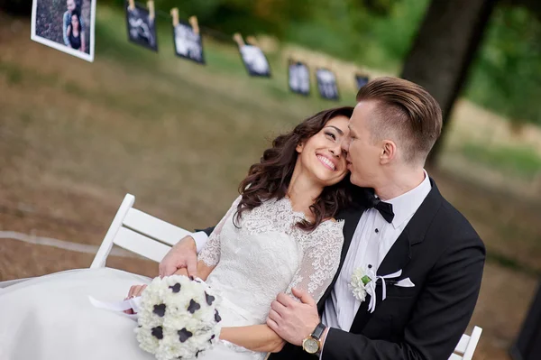 Felice sposa e lo sposo seduto sulla panchina nel parco — Foto Stock