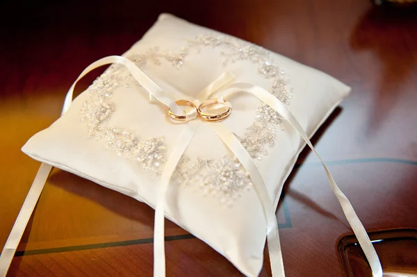 Два удивительных золотых блестящих кольца драгоценность для церемонии бракосочетания лежа на белой красивой подушке с луком — стоковое фото