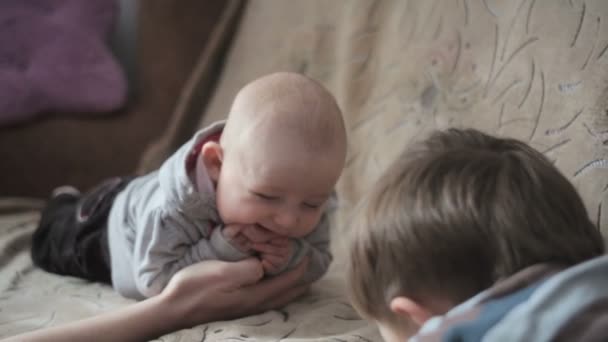 Młodszy brat i siostra leżąc na kanapie naprzeciw siebie — Wideo stockowe