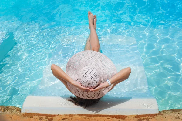 Pernas e um chapéu de mulher na água da piscina — Fotografia de Stock