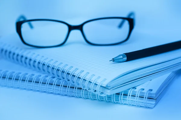 Lápiz negro y gafas que yacen en el cuaderno primer plano de color azul —  Fotos de Stock