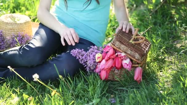 Schöne Frau sitzt auf dem Gras mit Korb voller Blumen — Stockvideo