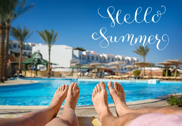 Pies descansando sobre un fondo de la piscina y letras Hello Summer — Foto de Stock