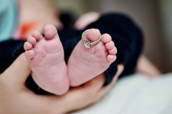 Newborns foot in the mother hand with wedding rings on finger — Stock Photo, Image