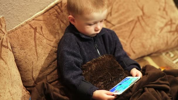 Маленький хлопчик дивиться мультфільм на смартфоні в приміщенні — стокове відео
