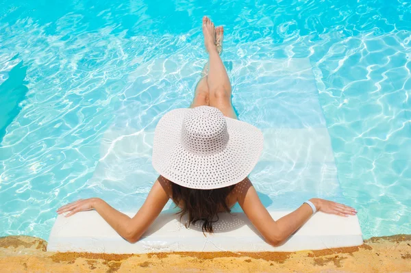 Hermosa mujer sombrero blanco y bikini tumbado en una piscina — Foto de Stock