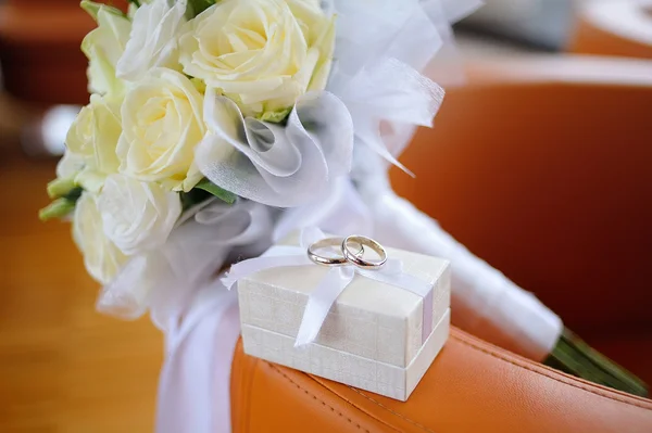 Caixa com anéis de casamento de ouro e um buquê de rosas brancas — Fotografia de Stock