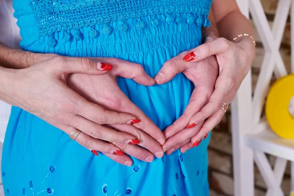 Gravid kvinna och hennes make hålla händerna i en hjärta form — Stockfoto