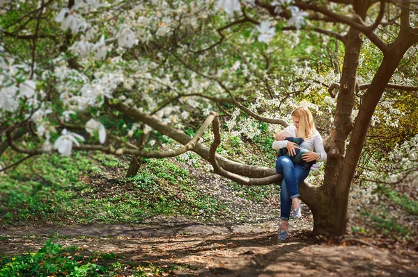 Mãe com o menino sentado no galho da árvore no jardim de primavera florido — Fotografia de Stock