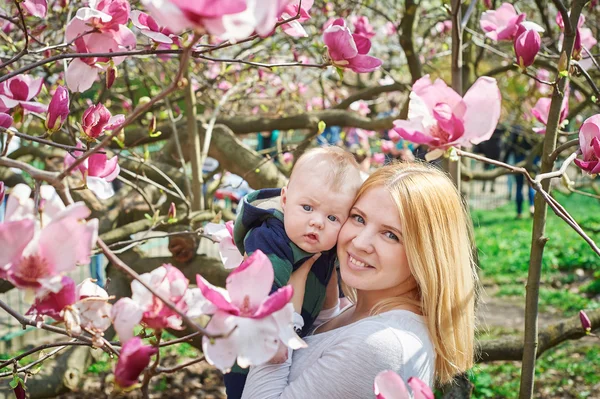 Mãe segurando bebê no jardim de magnólias florescendo — Fotografia de Stock