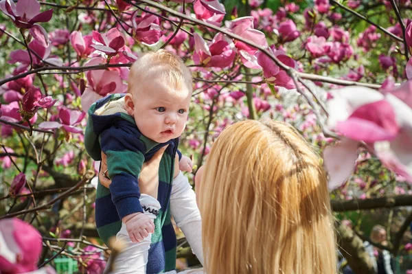 Mutter hält Baby im blühenden Magnoliengarten — Stockfoto