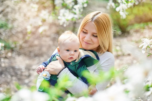 Liten pojke med sin unga mor i den blommande vår trädgården — Stockfoto