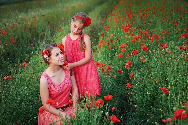 Zwei schöne junge Schwestern, die im Mohnfeld wandeln — Stockfoto