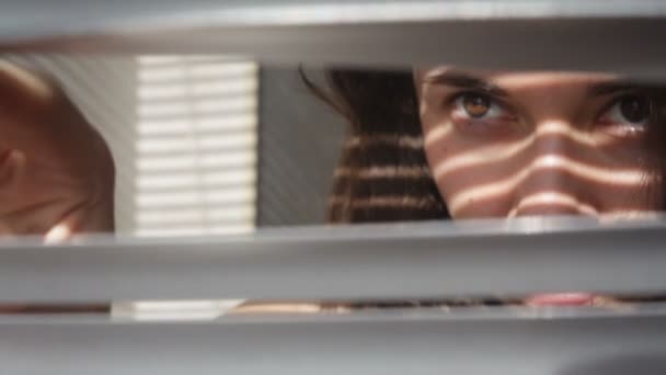 Женщина смотрит через жалюзи окна на улицу — стоковое видео