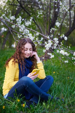 Bir akıllı telefon ile çimenlerin üzerinde oturan güzel genç kadın