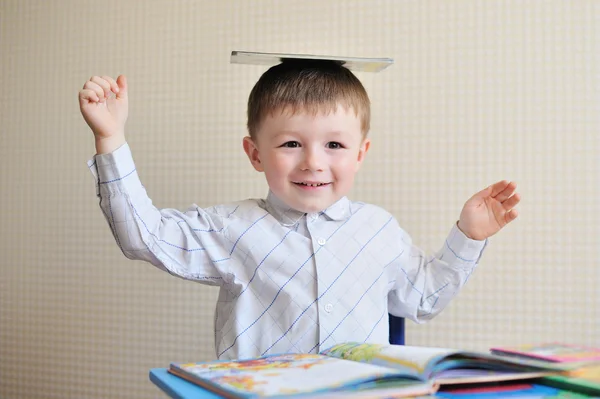 Young schoolboy playing with books and smiling as he sits at his desk in classroom — Stock Photo, Image