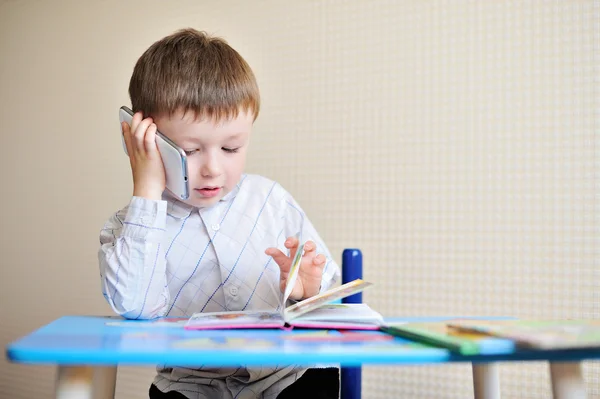 Little boy is sitting at a desk in school and speaking on the phone — Stock Photo, Image