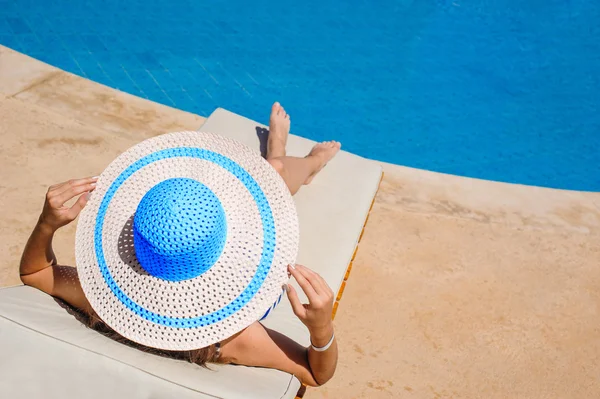 Mulher feliz com chapéu banhos de sol em uma espreguiçadeira junto à piscina — Fotografia de Stock