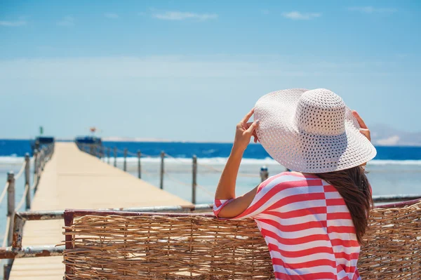 Closeup back view of woman in white hat looking out towards blue ocean and sky — Stock Photo, Image